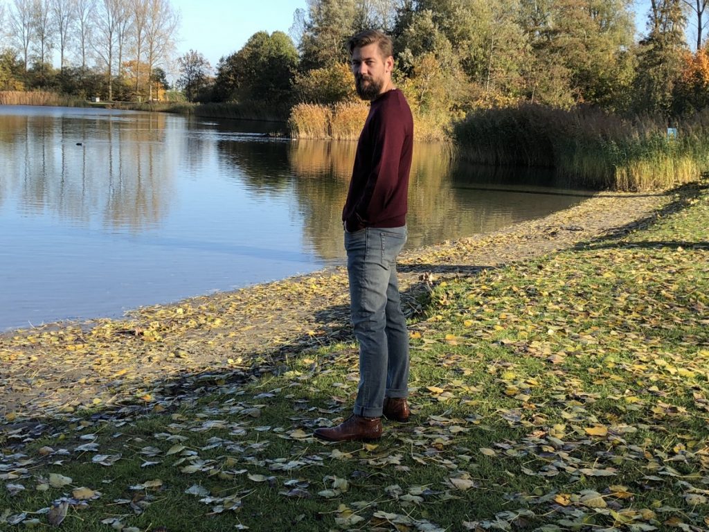 Jan Willem aan de rand van het water en draagt een casual outfit.