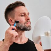 Man scheert zijn gezicht met een blauw scheermes en kijkt in een handspiegel.