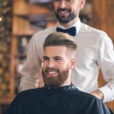 Glunderende man met perfect gestyled haar en een verzorgde baard bij de kapper, genietend van een frisse nieuwe look.