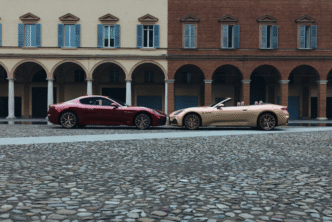 Twee exclusieve Maserati’s – de GranTurismo en GranCabrio Meccanica Lirica – staan neus aan neus op het plein in Modena, voor de historische Italiaanse arcades.