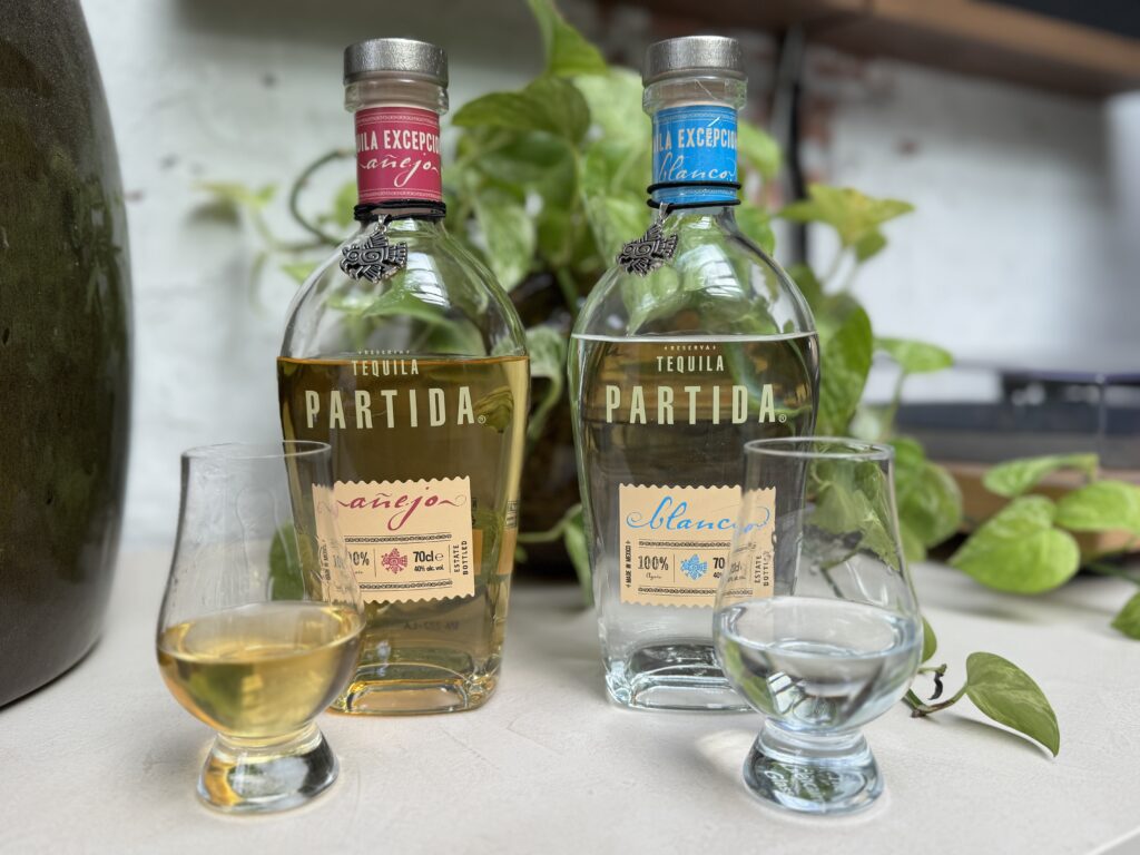 De twee flessen van Partida Tequila met twee gevulde glazen ernaast